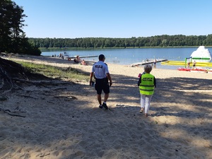 Policjant i pracownica Sanepidu idą w stronę jeziora