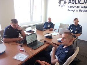 policjanci siedzą przy biurku i oglądają ekrany monitorów i telewizora