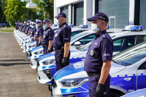 Policjanci stojący przy radiowozach w rzędzie.