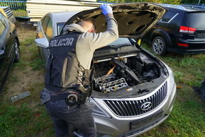 policjant trzyma maskę od samochodu do góry i zagląda do wnętrza silnika pojazdu