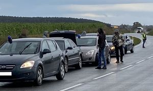 Rząd samochodów, przy których stoją policjanci.