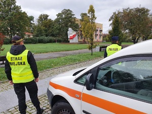 Policjant i strażnik miejski kontrolują tereny zielone w mieście.