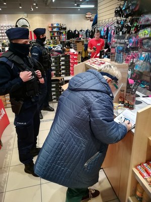 Kobieta w asyście policjantów sprawdza środki do dezynfekcji