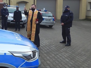 Kapłan święci pojazd. W tle pozostałe osoby uczestniczące w spotkaniu.