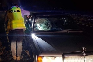 policjant stoi przy samochodzie, który ma zbitą przednią szybę