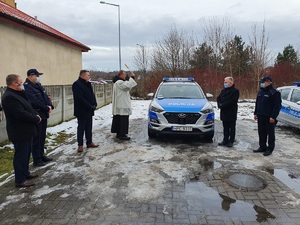 Ksiądz święci radiowóz w obecności pozostałych uczestników spotkania.