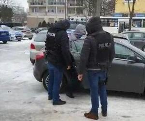 Zatrzymany wsiada do policyjnego radiowozu nieoznakowanego. Stoją przy nim policjanci.