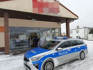 policjant wchodzi do marketu. Przed budynkiem stoi radiowóz