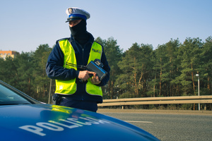 Policjant stoi przy radiowozie trzymając w ręku miernik prędkości