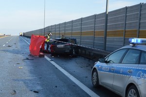 Widok na autostradę i policjanta stojącego nad rozbitym samochodem