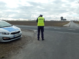 Policjant stoi przy drodze i wykonuje pomiar prędkości