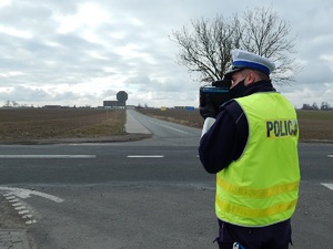 Policjant stoi przy drodze i wykonuje pomiar prędkości