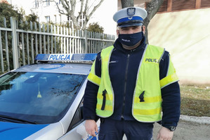 Policjant pozuje do zdjęcia na tle radiowozu