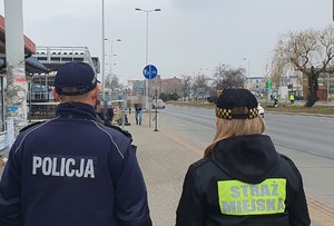 Policjant i strażniczka miejska stoją na chodniku