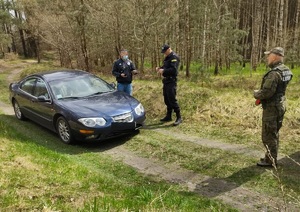 Policjant i strażnik leśny kontrolują zatrzymany w lesie samochód