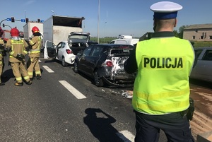 Policjant &quot;drogówki&quot; robi zdjęcie stłuczonych aut stojących po prawej stronie,a obok grupka strazaków.