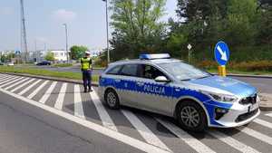 Policjant stoi obok radiowozu i monitoruje prędkość poruszających się aut