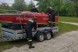 Strażacy i policjant stoją przy łodzi