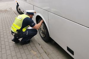 Policjant kontroluje stan ogumienia autobusu