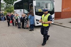 Idący policjant na tle autobusu i dzieci