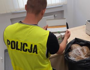 Policjant eksponuje nielegalne papierosy, a obok leży tytoń