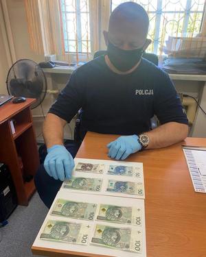 Policjant siedzi przy biurku, a przed nim leżą zabezpieczone banknoty