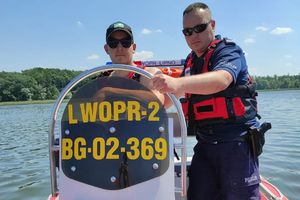 Policjant pozuje do zdjęcia na łodzi wraz z ratownikiem WOPR