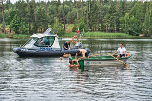 policjant wyciąga mężczyznę z wody na łódź policyjna i inny policjant wyciąga mężczyznę na łódkę z wiosłami