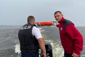 Policjant z WOPR-owcem na łodzi, a za nimi holowana motorówka