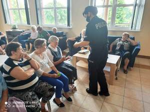 policjantka podchodzi do seniorów siedzących na krzesłach