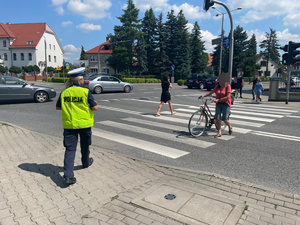 Policjantka w okolicy przejścia dla pieszych podchodzi do idącej kobiety, która prowadzi rower