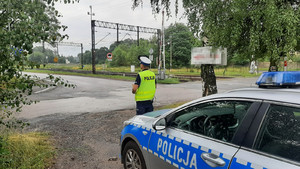 Policjant RD stoi obok radiowozu i prowadzi działania &quot;Bezpieczny przejazd&quot;