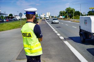 Policjant stoi przy drodze i wykonuje pomiar prędkości