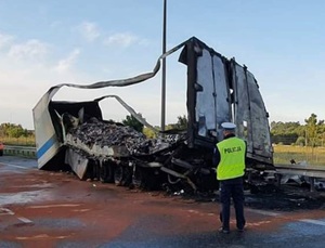 Policjant stoi obok spalonej ciężarówki