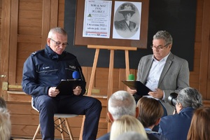 Komendant policji i mężczyzna siedząc na krzesłach czytają książkę.