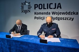 Komendant Komendy Wojewódzkiej Policji w Bydgoszczy i Główny Inspektor Ochrony Środowiska siedzą przy stole i podpisują dokumenty