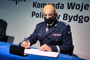 Komendant Komendy Wojewódzkiej Policji w Bydgoszczy siedząc przy stole i trzymając w ręku długopis patrzy w stronę obiektywu