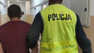 Policjant prowadzi korytarzem sprawcę