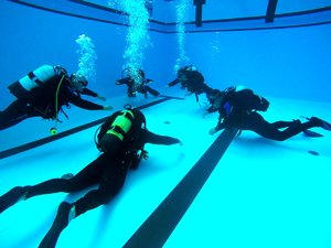 Zdjęcie przedstawia policjantów podczas praktycznego szkolenia nurkowego na basenie i wodach otwartych.