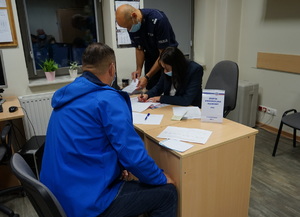 Mężczyzna podczas spisywania dokumentów przy biurku z pracownikami kwp.
