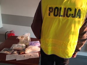Policjant stoi przy biurku, na którym leża zabezpieczone środki