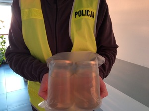 Policjant trzyma zabezpieczone dwa słoiki z płynem o właściwościach narkotycznych