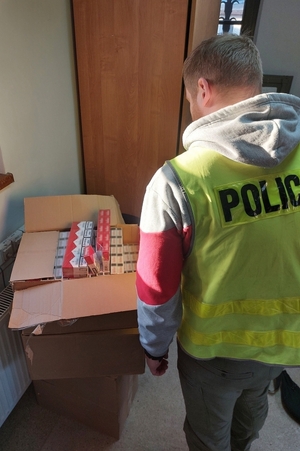 Policjant stoi przy zabezpieczonych paczkach papierosów