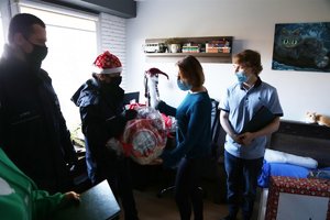 Policjanci stoją w pokoju chłopca, jego Mama odbiera od policjantki kosz ze słodyczami i krasnala