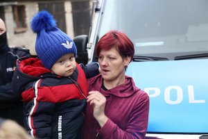 Kobieta trzyma swoje dziecko na ręku, w tle radiowóz