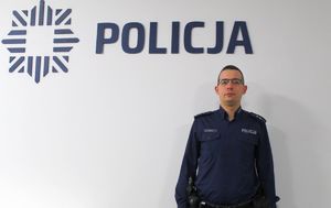 policjant stoi przy ścianie na tle napisu Policja