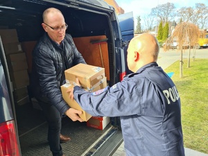policjant podaje paczkę mężczyźnie, który znajduje się w części bagażowej pojazdu dostawczego