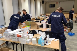 na stołach leżą zebrane artykuły medyczne a obok stoją policjanci, którzy przygotowują paczki