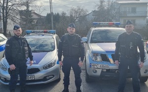 trzej umundurowani policjanci stoją przed radiowozami