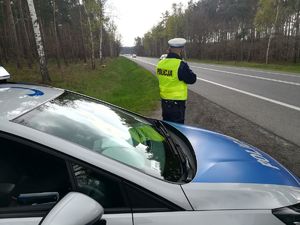 Policjant stoi obok radiowozu i mierzy prędkość